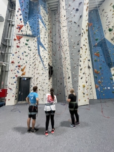 Zwei Teilnehmende und ein Trainer stehen vor der Kletterwand
