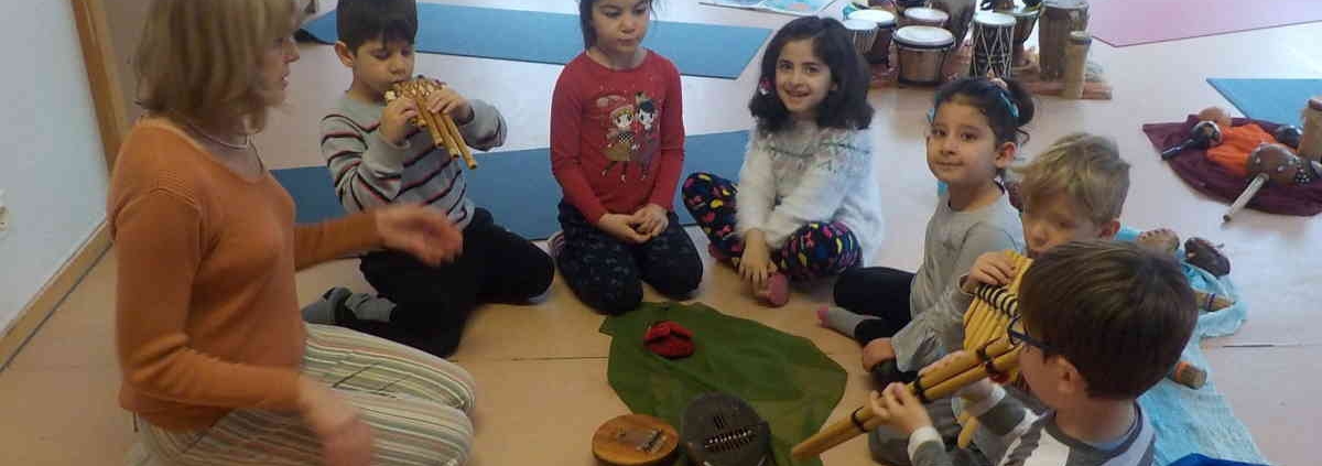 Kinder und Kursleiterin sitzen im Halbkreis auf dem Boden, die Kinder sehen aufmerksam zur Leiterin hin
